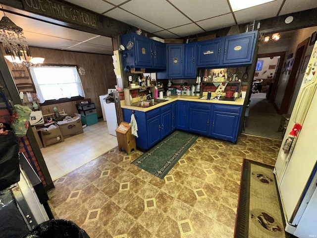 kitchen featuring a drop ceiling, blue cabinets, wooden walls, and an inviting chandelier