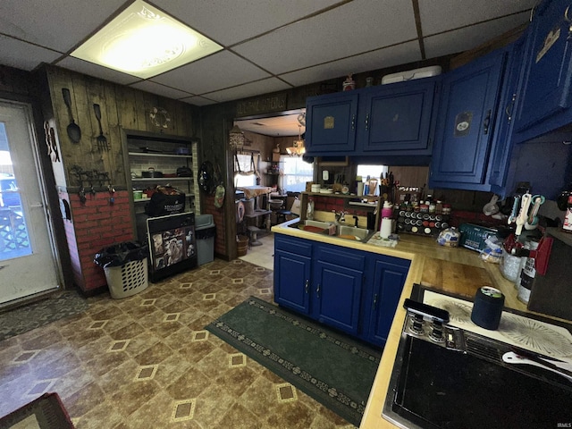 kitchen with a paneled ceiling, wood walls, blue cabinets, sink, and cooktop