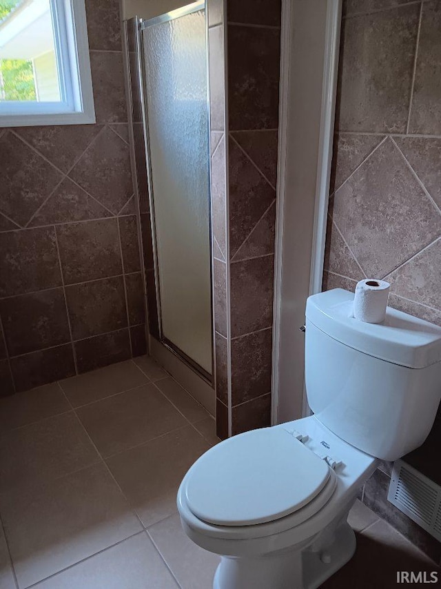 bathroom featuring tile patterned floors, toilet, walk in shower, and tile walls