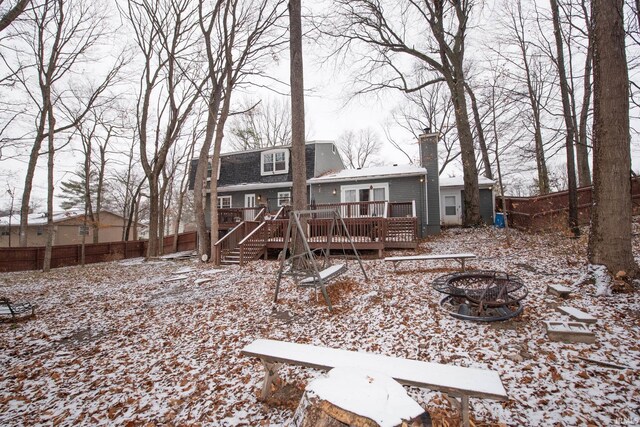 snow covered rear of property with a wooden deck and an outdoor fire pit