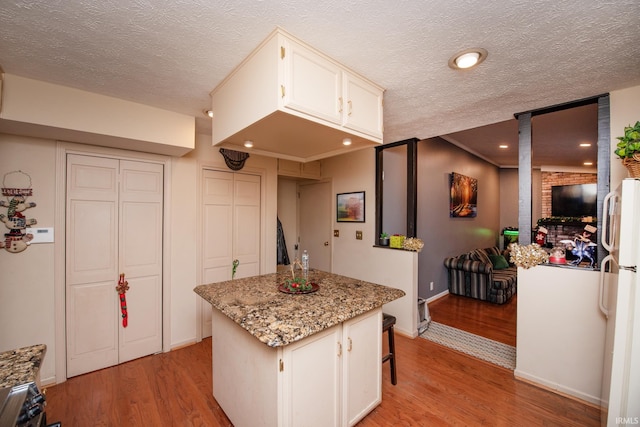 kitchen featuring a center island, white refrigerator, light stone countertops, a textured ceiling, and light hardwood / wood-style floors