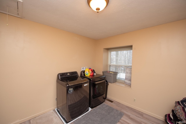 clothes washing area featuring washing machine and clothes dryer, light hardwood / wood-style floors, and a textured ceiling