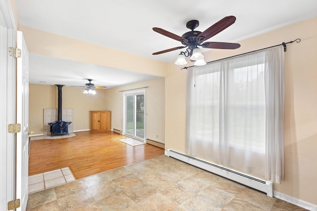 unfurnished living room with ceiling fan, light hardwood / wood-style floors, a wood stove, and a baseboard radiator