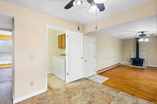 unfurnished living room with a wood stove, light hardwood / wood-style flooring, ceiling fan, a baseboard radiator, and washing machine and clothes dryer