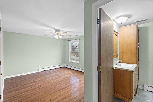 interior space featuring hardwood / wood-style floors, vanity, ceiling fan, and a baseboard heating unit