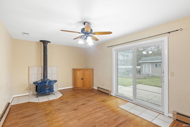 unfurnished living room with a wood stove, light hardwood / wood-style floors, and a baseboard radiator