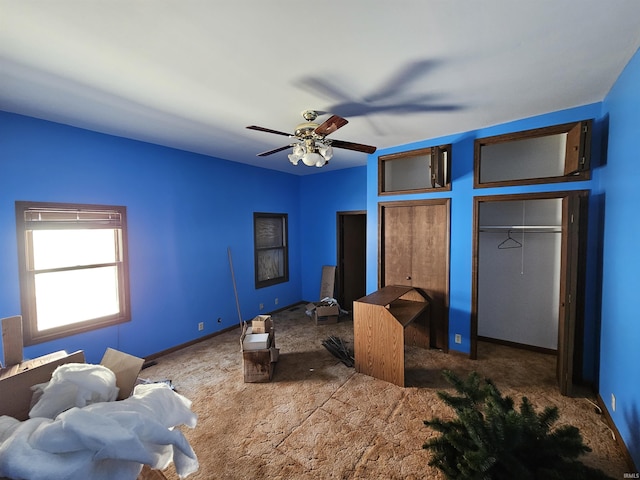 bedroom featuring ceiling fan, dark carpet, and multiple closets