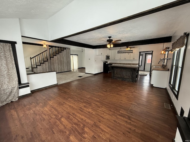 unfurnished living room with a textured ceiling, ceiling fan, sink, and dark wood-type flooring