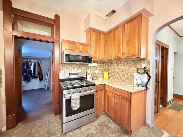 kitchen featuring light stone countertops, backsplash, appliances with stainless steel finishes, and light hardwood / wood-style flooring