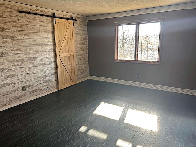 empty room featuring wood walls, a barn door, dark hardwood / wood-style flooring, and crown molding