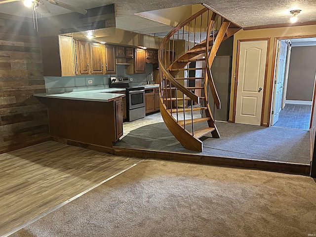 kitchen featuring a textured ceiling, sink, light hardwood / wood-style flooring, stainless steel electric range oven, and wood walls