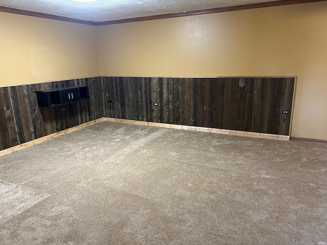 carpeted spare room featuring a textured ceiling, ornamental molding, and wood walls