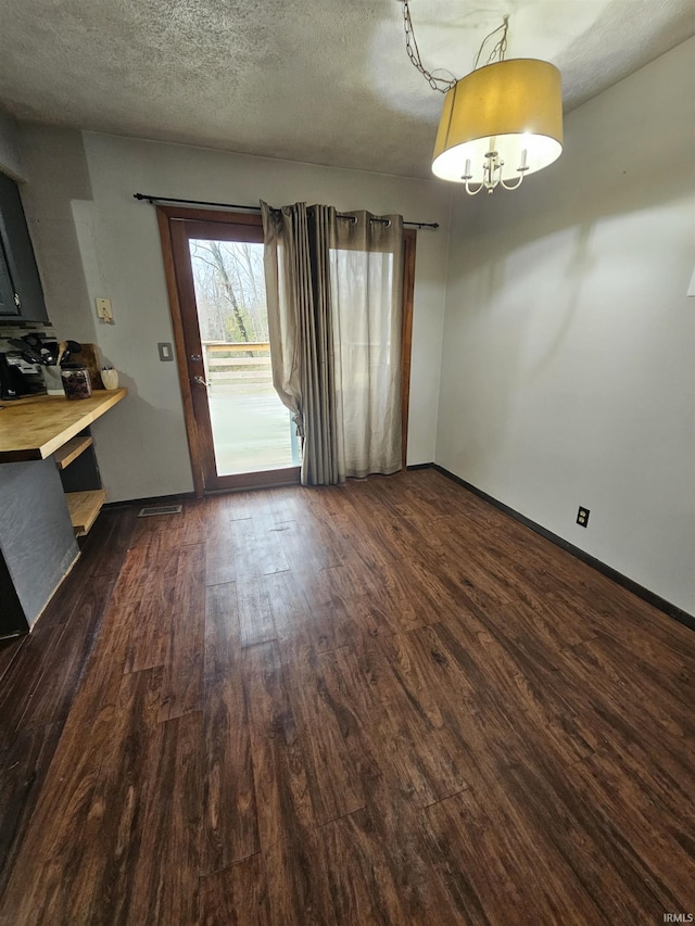 unfurnished dining area with dark wood-type flooring and a textured ceiling