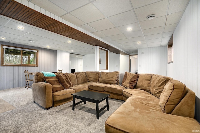 carpeted living room featuring a drop ceiling and wood walls