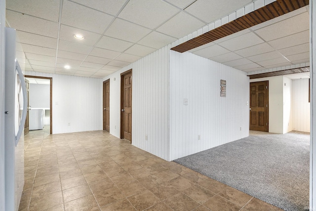 carpeted spare room featuring a paneled ceiling and wood walls