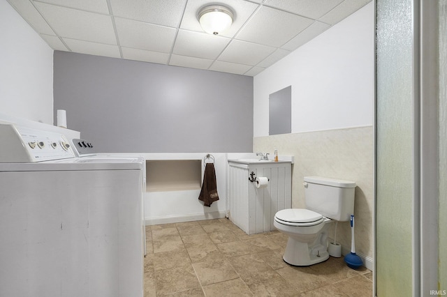 bathroom featuring washer and dryer, vanity, toilet, and a drop ceiling