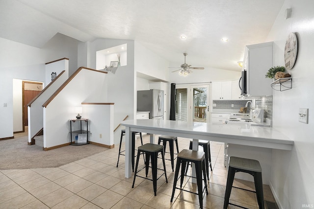 kitchen featuring kitchen peninsula, stainless steel appliances, vaulted ceiling, ceiling fan, and white cabinets