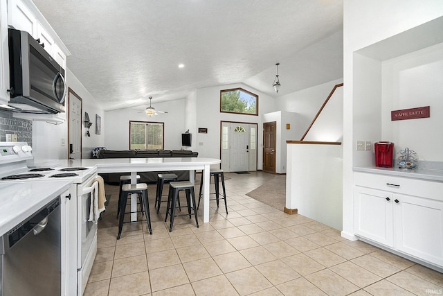 kitchen with white cabinets, vaulted ceiling, ceiling fan, light tile patterned floors, and appliances with stainless steel finishes