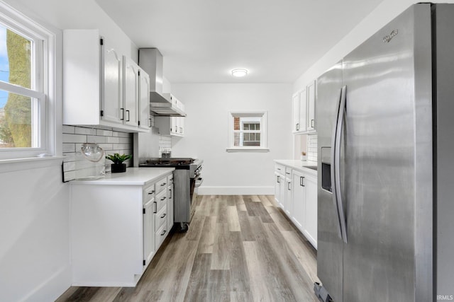 kitchen with wall chimney range hood, light hardwood / wood-style flooring, tasteful backsplash, white cabinetry, and stainless steel appliances