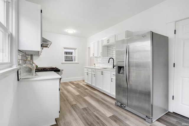 kitchen with white cabinetry, sink, wall chimney range hood, stainless steel fridge, and light wood-type flooring