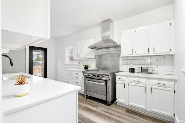 kitchen featuring stainless steel stove, white cabinetry, wall chimney exhaust hood, and sink