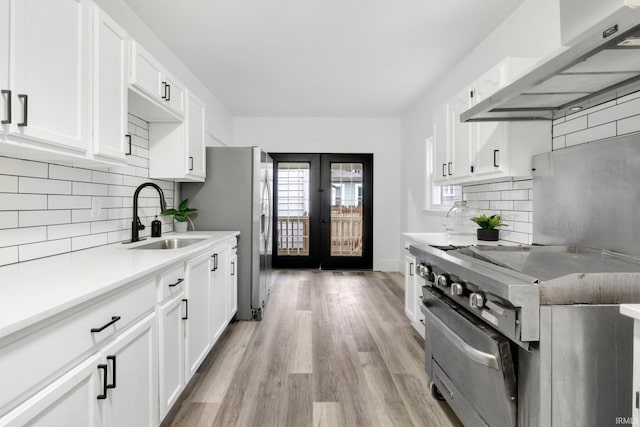 kitchen featuring white cabinetry, stainless steel stove, sink, and range hood