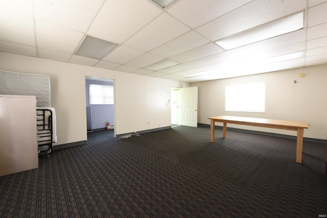 basement with a drop ceiling, a healthy amount of sunlight, and dark carpet