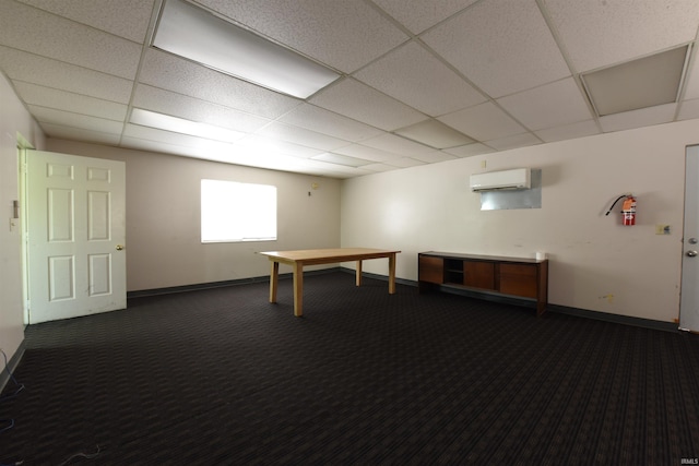 recreation room featuring a paneled ceiling, a wall mounted air conditioner, and dark colored carpet