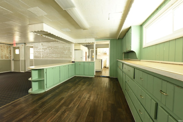 kitchen with wood walls, green cabinetry, dark hardwood / wood-style floors, white fridge, and brick wall