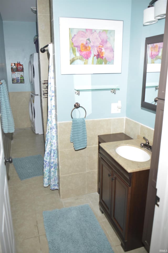 bathroom featuring vanity, stacked washing maching and dryer, tile patterned floors, and tile walls