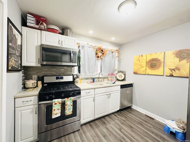 kitchen with white cabinetry, sink, stainless steel appliances, backsplash, and light wood-type flooring