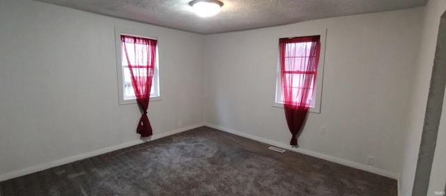 spare room with a healthy amount of sunlight, a textured ceiling, and dark colored carpet