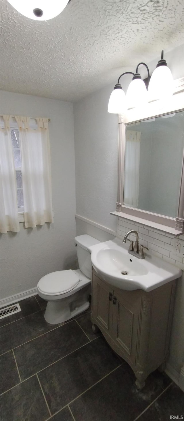 bathroom featuring a textured ceiling, vanity, toilet, and backsplash