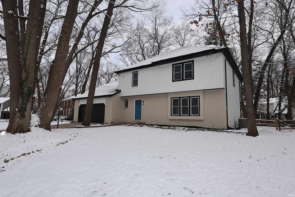 snow covered back of property with cooling unit and a garage