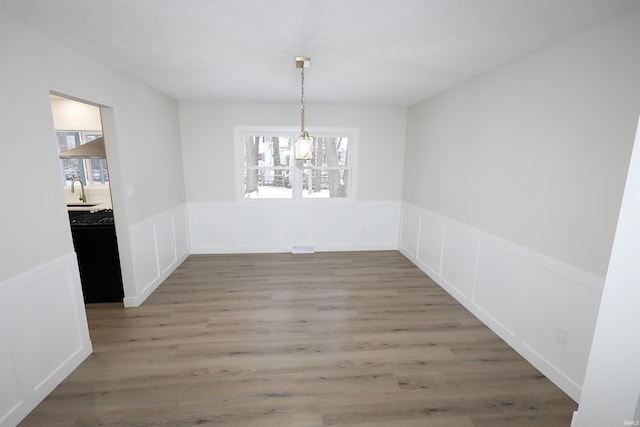 unfurnished dining area with hardwood / wood-style floors, an inviting chandelier, and sink