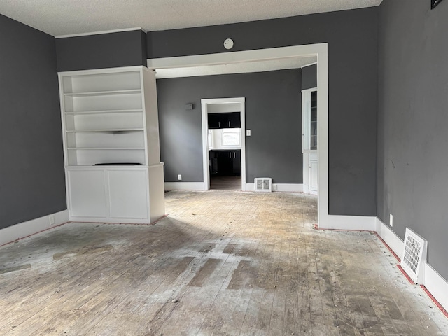 empty room featuring wood-type flooring, a textured ceiling, and built in shelves