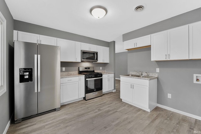 kitchen featuring white cabinets, sink, light stone countertops, light wood-type flooring, and stainless steel appliances