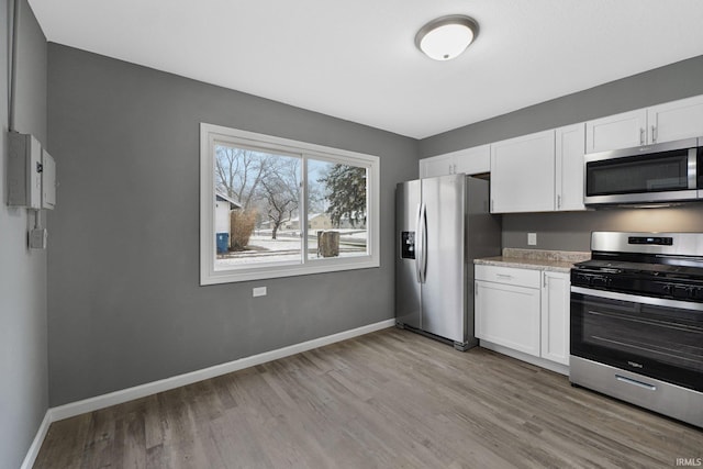 kitchen with light stone counters, white cabinets, light hardwood / wood-style floors, and appliances with stainless steel finishes