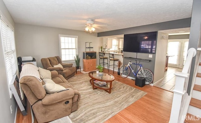 living room featuring ceiling fan, light hardwood / wood-style floors, and a textured ceiling