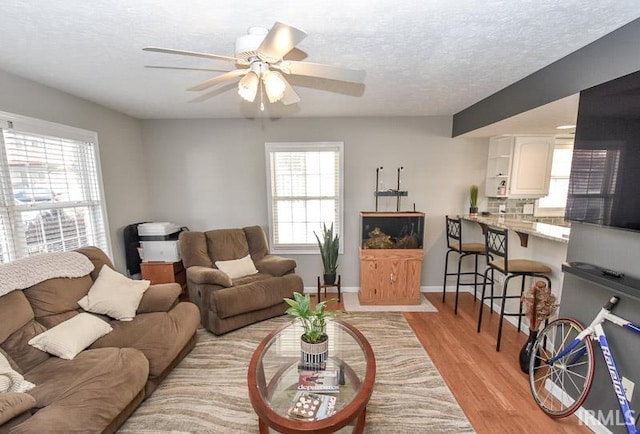 living room with ceiling fan, light hardwood / wood-style flooring, and a textured ceiling