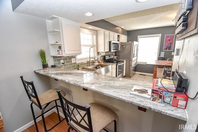 kitchen featuring a kitchen breakfast bar, white cabinetry, light stone counters, and appliances with stainless steel finishes