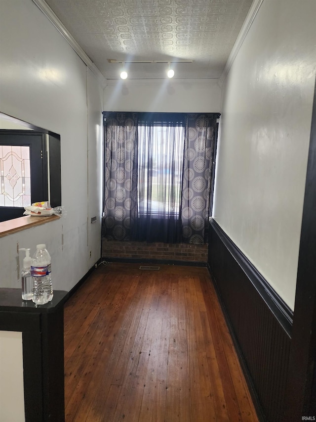 unfurnished room with a textured ceiling, dark wood-type flooring, track lighting, and crown molding