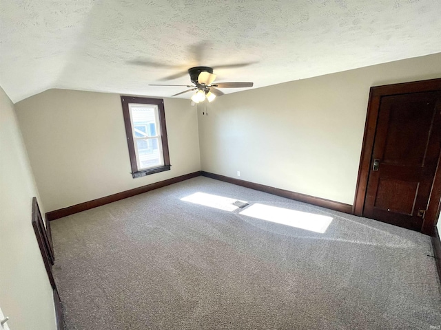 interior space with a textured ceiling, carpet floors, vaulted ceiling, and ceiling fan