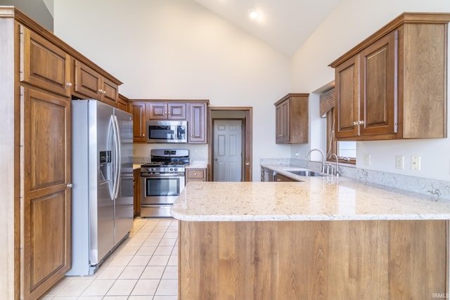 kitchen featuring kitchen peninsula, stainless steel appliances, light stone counters, and sink