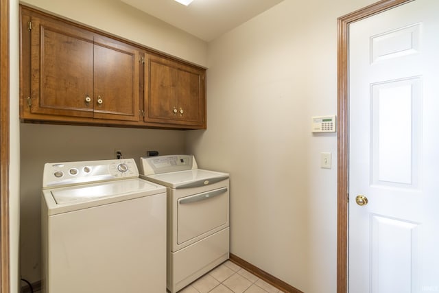 clothes washing area with washing machine and dryer, light tile patterned flooring, and cabinets