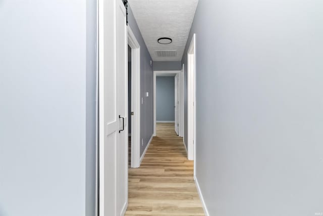 hallway featuring a barn door, light hardwood / wood-style flooring, and a textured ceiling