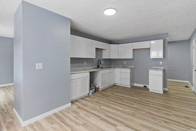 kitchen featuring white cabinets, a textured ceiling, light hardwood / wood-style flooring, and sink