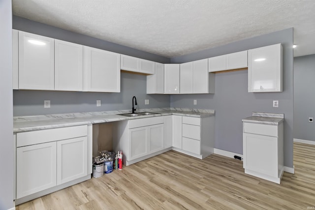 kitchen with white cabinets, a textured ceiling, sink, and light hardwood / wood-style flooring