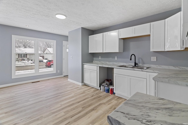 kitchen with white cabinetry, sink, light stone counters, light hardwood / wood-style floors, and a textured ceiling