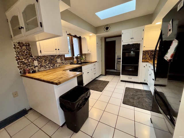 kitchen featuring white cabinets, black appliances, sink, a skylight, and butcher block counters